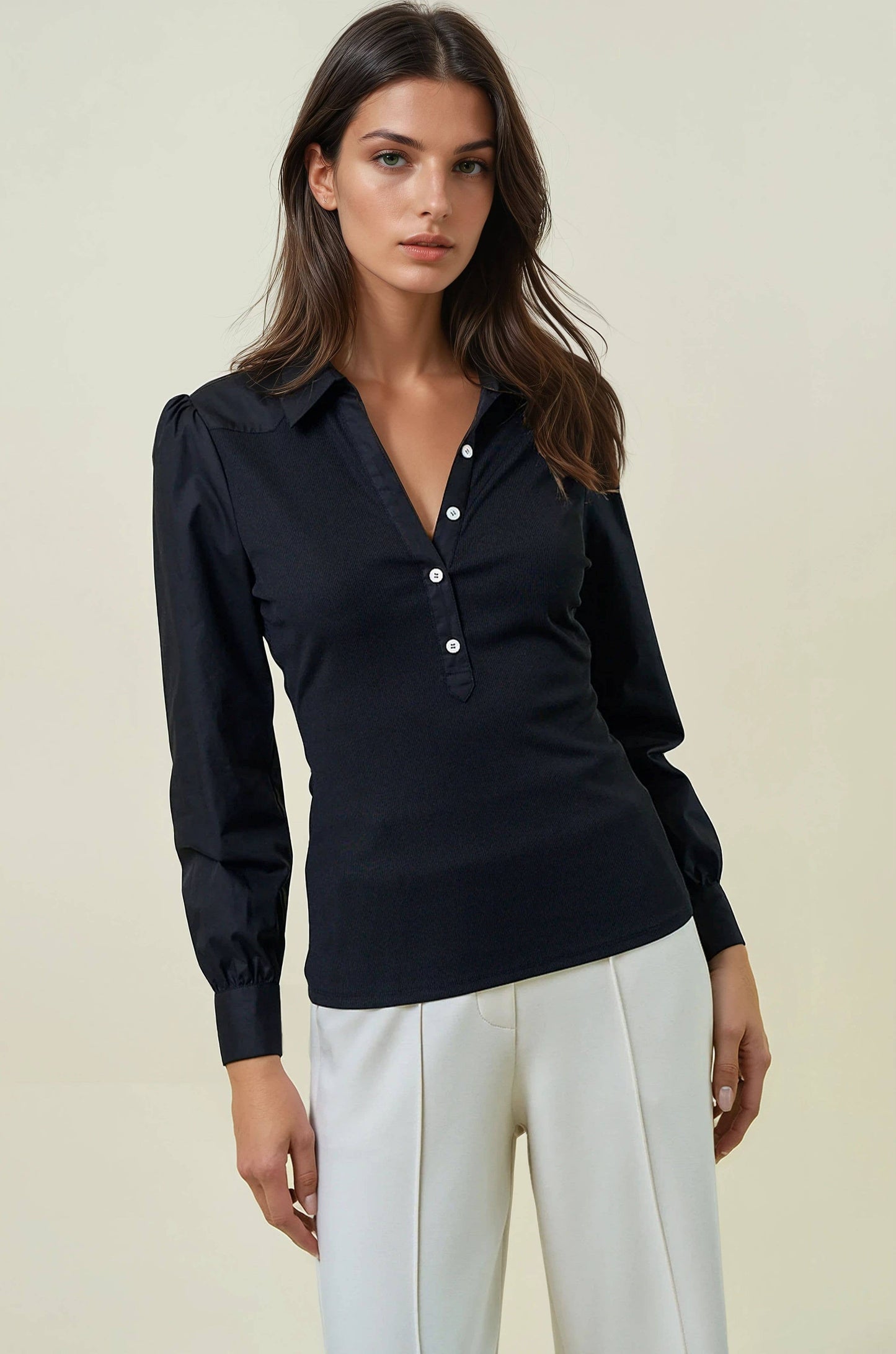 Woman wearing a black long-sleeve shirt with white buttons and white pants on a beige background