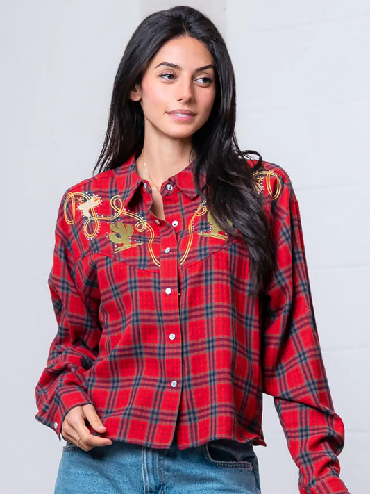 Woman wearing a red plaid shirt with embroidery on a plain background