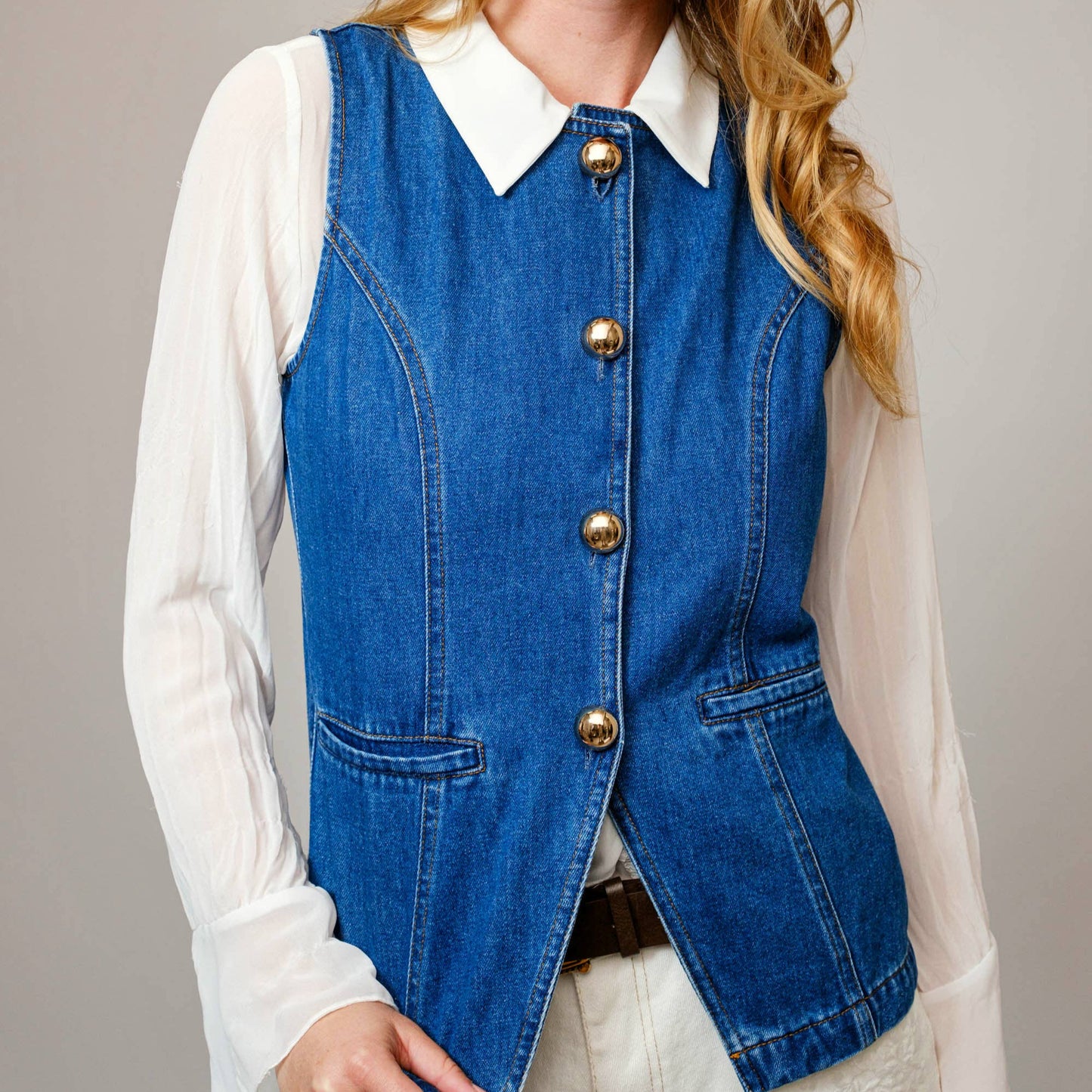 Woman wearing a blue denim vest over a white shirt on a plain background