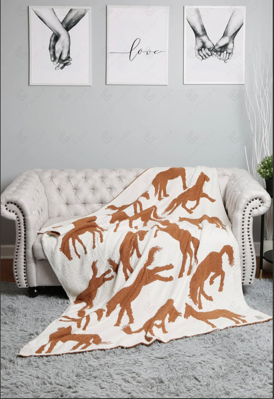 A blanket with horse patterns draped over a couch in a room with artwork on the walls.