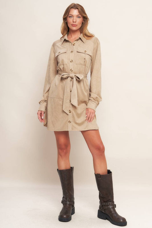 Woman wearing a beige dress with a belt and dark boots on a white background