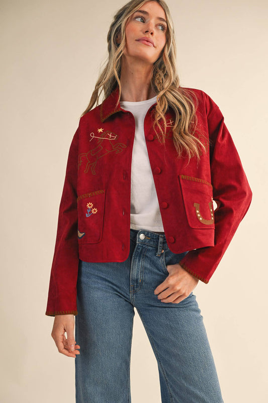 Woman wearing a red jacket with embroidery, white shirt, and blue jeans on a beige background