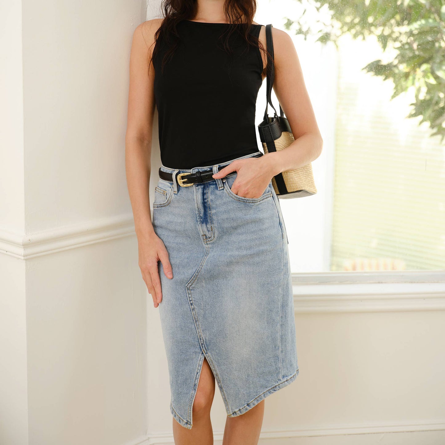 Woman wearing a black sleeveless top and denim skirt standing indoors.