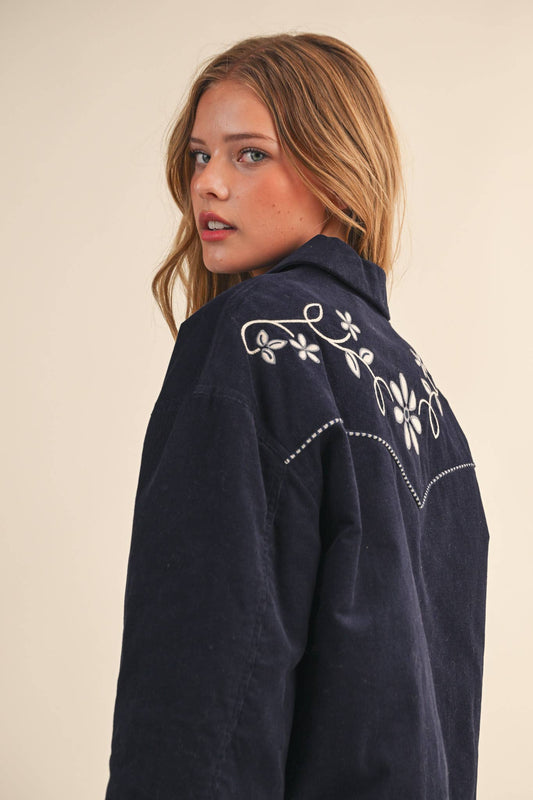 Woman wearing a navy blue embroidered jacket on a beige background