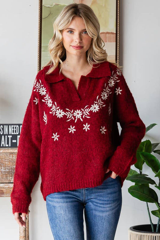 Woman wearing a red sweater with white floral patterns indoors.