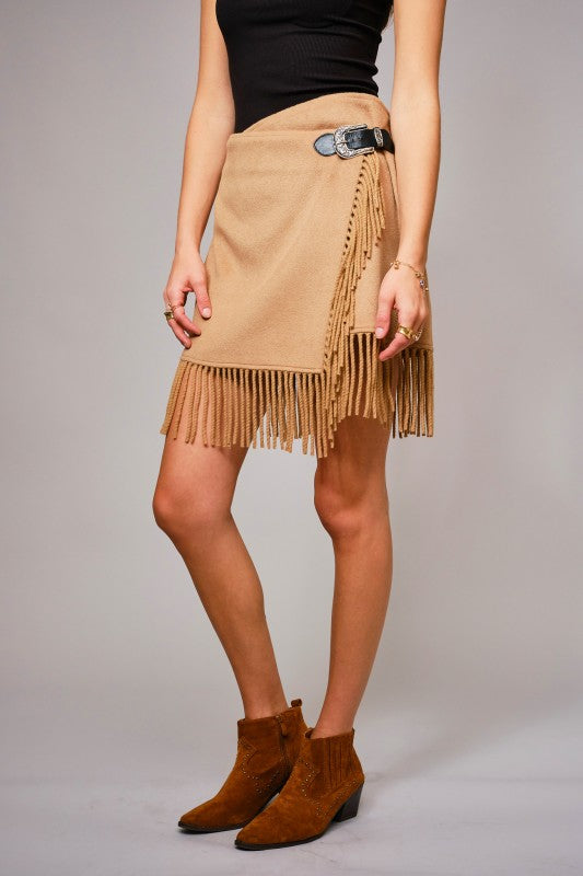 Person wearing a beige fringed skirt with a plain background