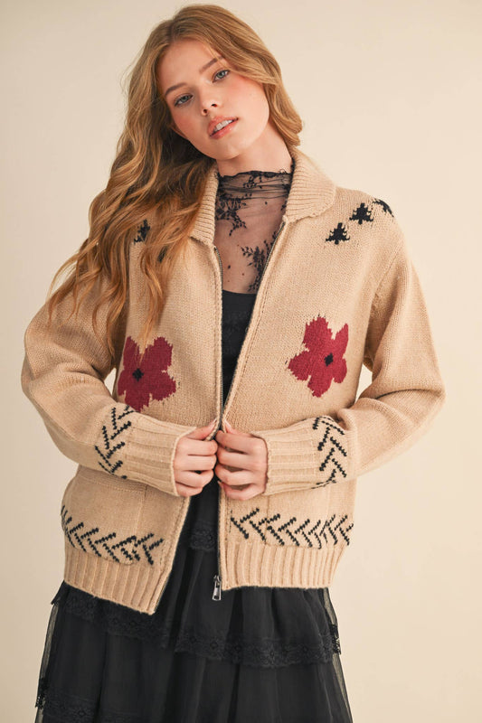 Woman wearing a beige sweater with red floral patterns on a plain background