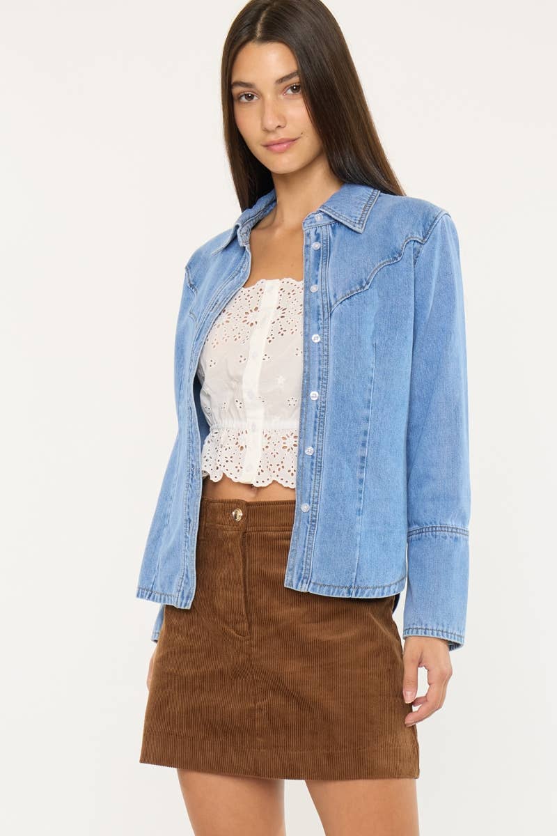 Woman wearing a denim jacket over a white lace top and brown skirt on a white background