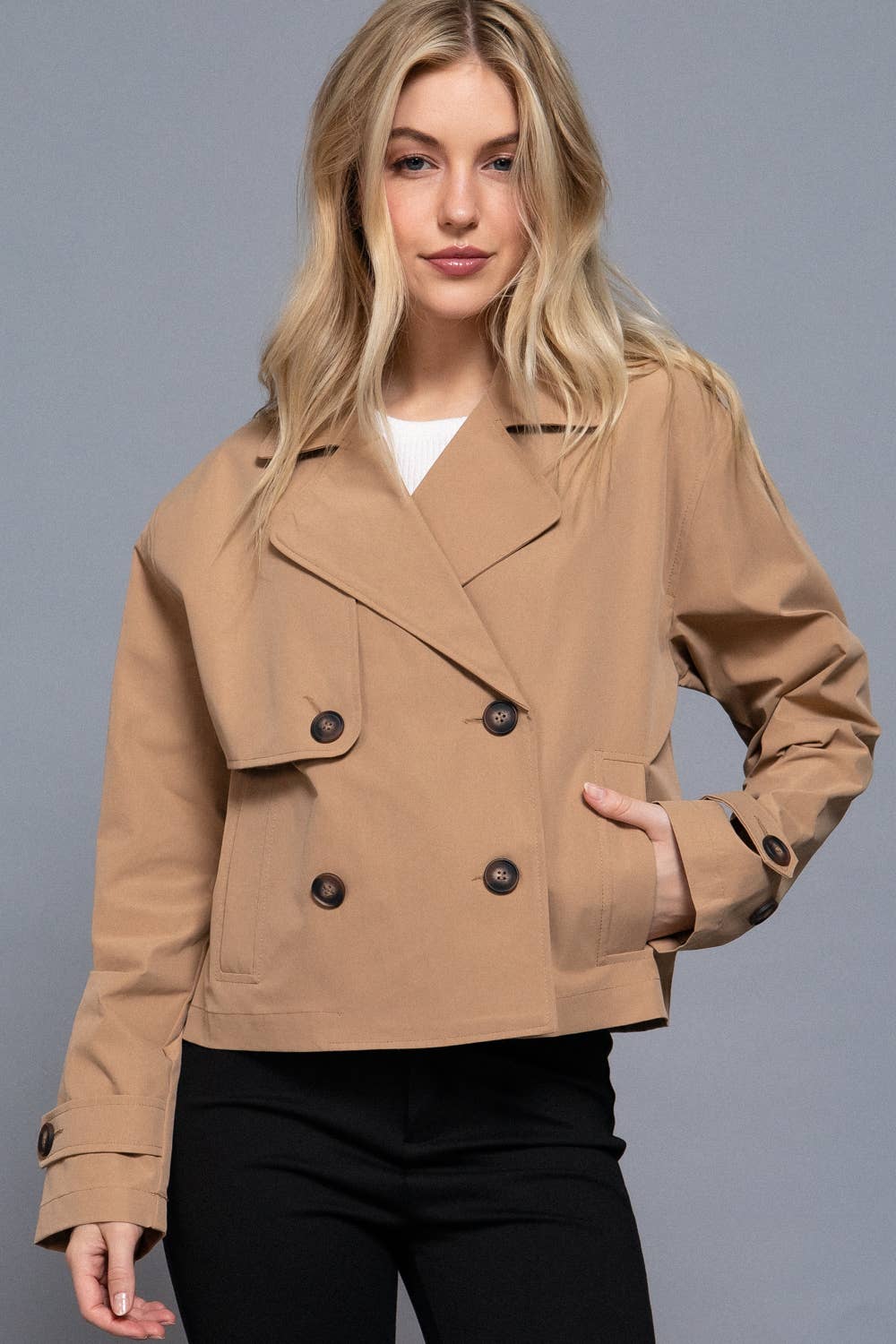 Woman wearing a tan jacket with black buttons on a gray background