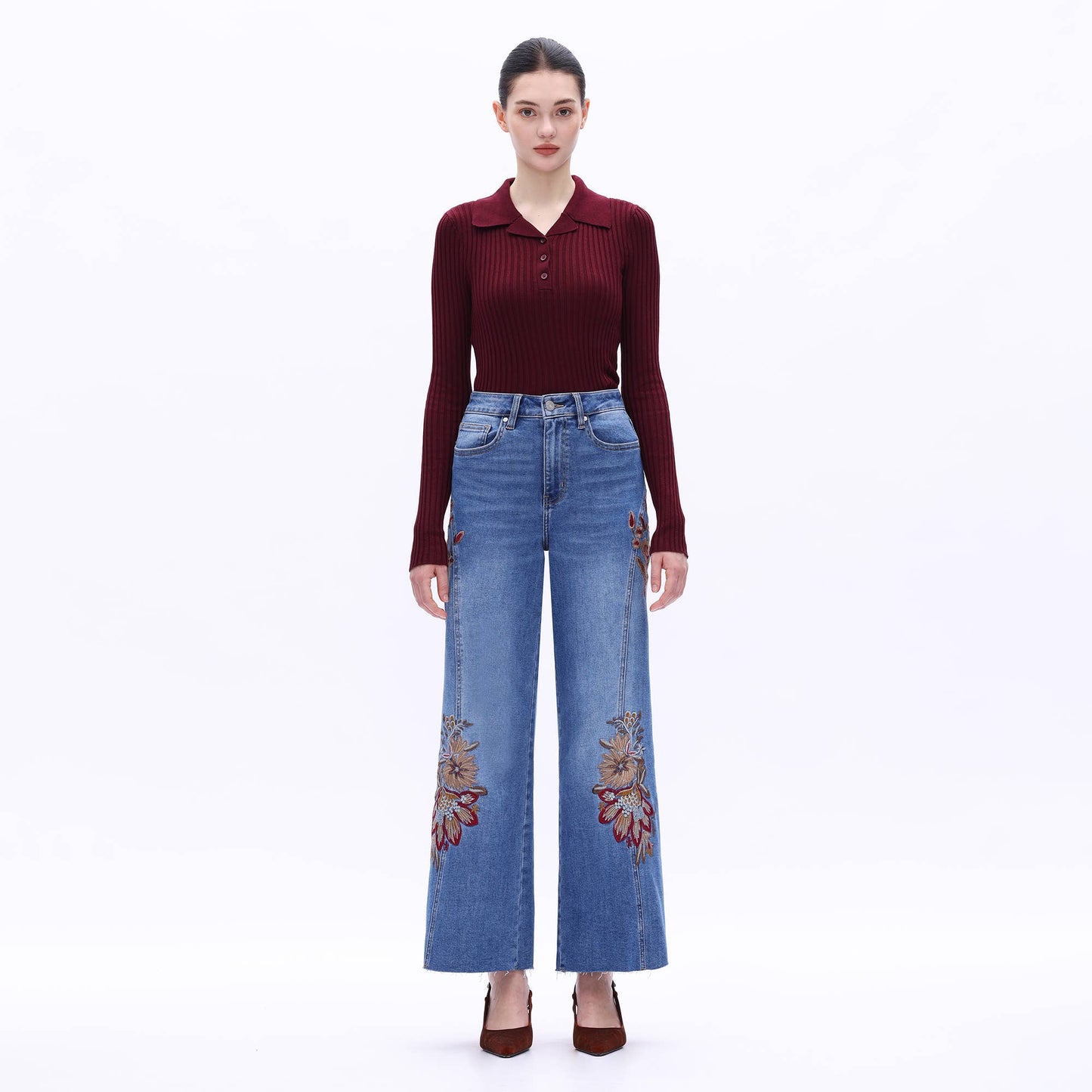 Woman wearing a burgundy top and blue jeans with floral embroidery on a white background