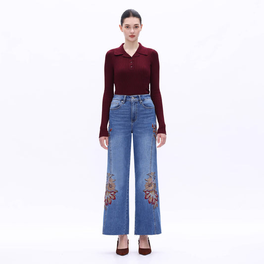 Woman wearing a burgundy top and blue jeans with floral embroidery on a white background