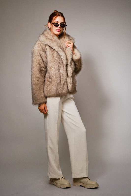 Person wearing a fur coat and sunglasses against a plain background