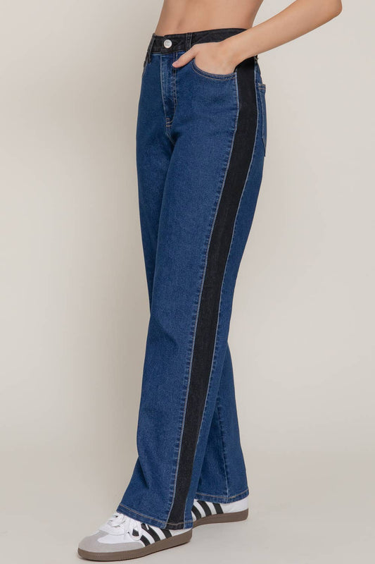 Blue jeans with black side stripes worn by a person on a beige background