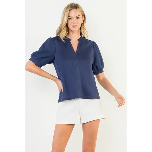 Woman wearing a navy blue blouse and white shorts on a white background