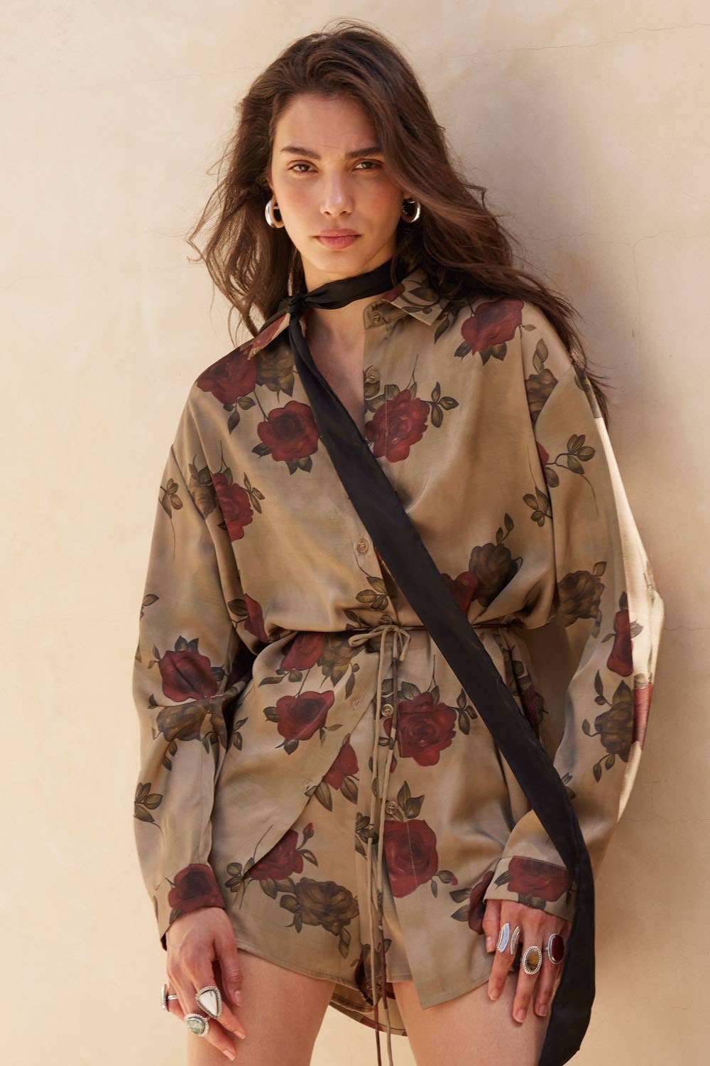 Woman wearing a floral dress with a black strap over her shoulder against a neutral background