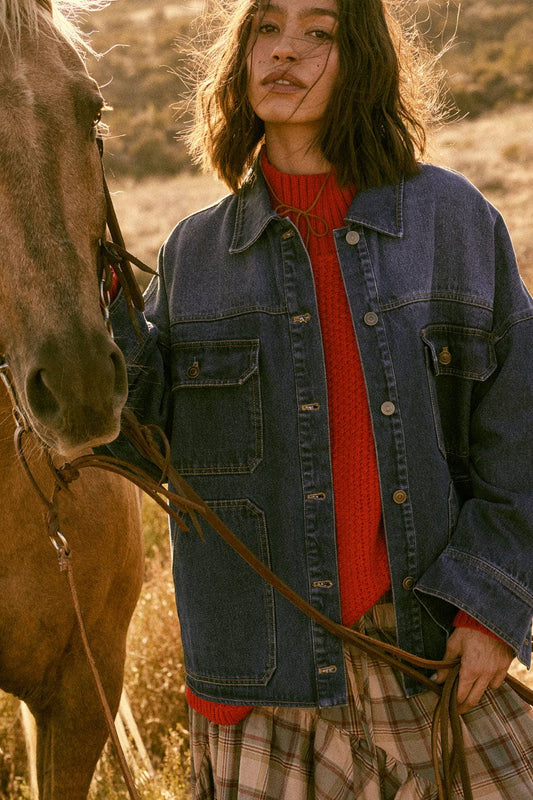 Woman in a denim jacket and red sweater standing next to a horse in a natural setting