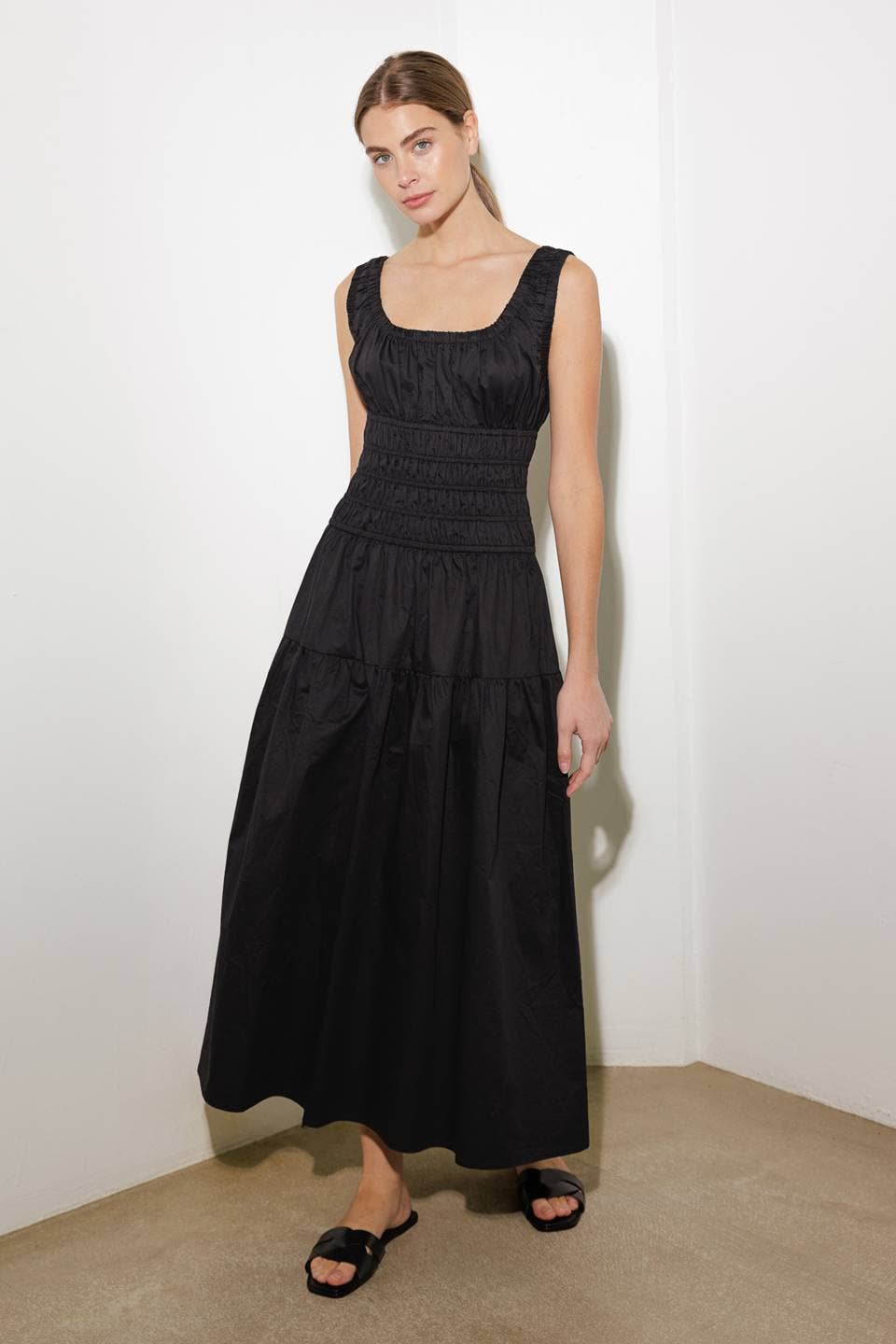 Woman wearing a black dress standing against a white wall.