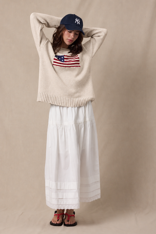 Taupe knit sweater with American flag graphic, paired with white maxi skirt and NY cap
