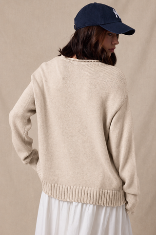Taupe knit crewneck sweater with ribbed hem, worn with white skirt and navy cap