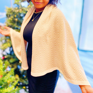 Camel herringbone knit poncho wrap with cream border, worn over black dress