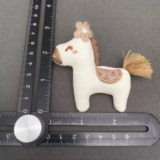 Small white linen-cotton horse brooch with brown mane, flower accent, and gold tassel tail