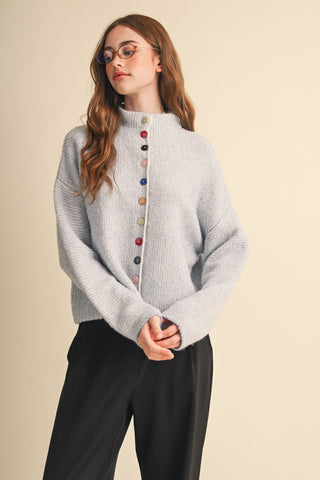 Powder blue knit cardigan with multicolored buttons and mock neck, styled with black trousers