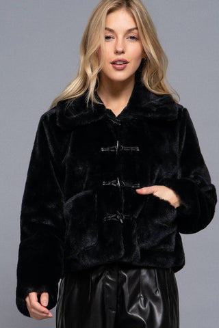 Black faux fur duffle jacket with toggle closures and wide collar worn over leather pants
