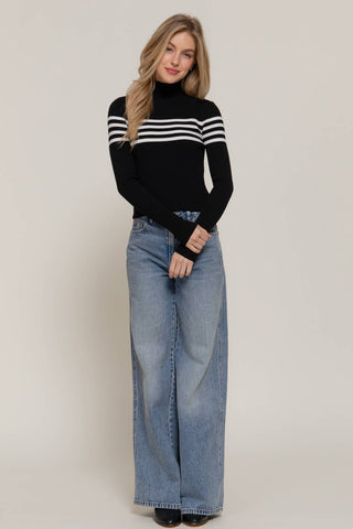 Black turtleneck sweater with white chest stripes, long sleeves, paired with wide-leg jeans