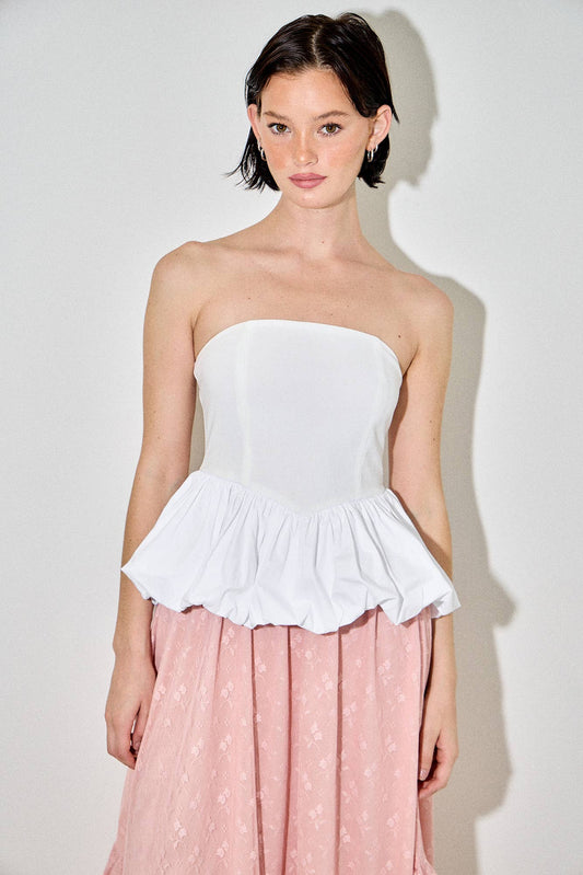 Woman wearing a white strapless top with a peplum waist and a pink skirt against a white background