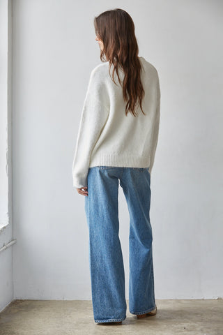 Cream oversized knit ski sweater paired with wide-leg blue jeans, back view