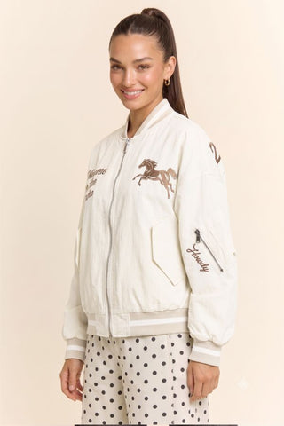 Cream bomber jacket with horse embroidery, script text, and ribbed cuffs and hem