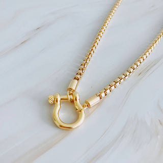 Ellison+Young gold box chain necklace with horseshoe shackle clasp on marble surface