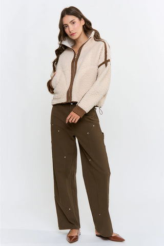 Cream sherpa zip-up jacket with brown contrast trim, worn with olive wide-leg pants