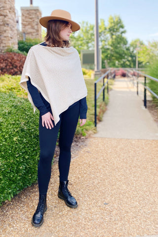 Cream herringbone knit poncho draped over black long-sleeve top and leggings
