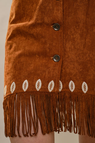 Tan suede mini dress with fringe hem, white embroidery, and button front