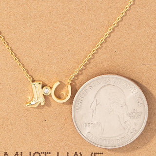 Gold-tone cowboy boot and horseshoe charm necklace with crystal accent, shown beside quarter for scale