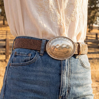 Brown floral embossed vegan leather belt with large silver hammered oval buckle on jeans