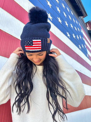 Navy ribbed knit beanie with American flag chenille patch and black faux fur pom