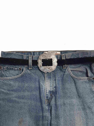 Black suede leather belt with large silver floral engraved western buckle on blue jeans