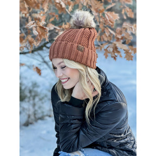 Rust orange knit CC beanie with faux fur pom pom on smiling blonde woman outdoors