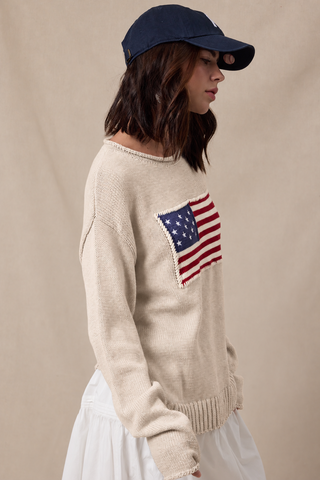 Taupe knit sweater with American flag graphic, worn with white skirt and navy cap