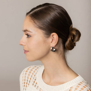 Chunky silver half hoop post earrings worn by a model with a low bun
