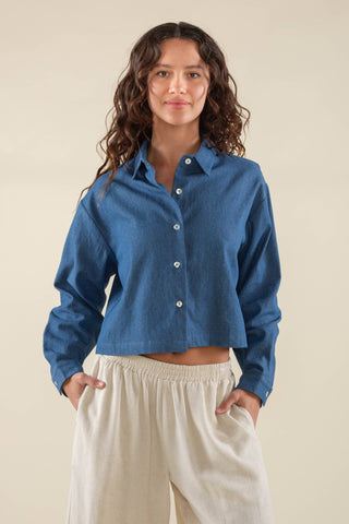Woman wearing a blue shirt and beige pants against a beige background