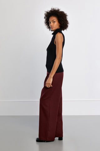 Black sleeveless turtleneck knit sweater worn with wide-leg burgundy trousers