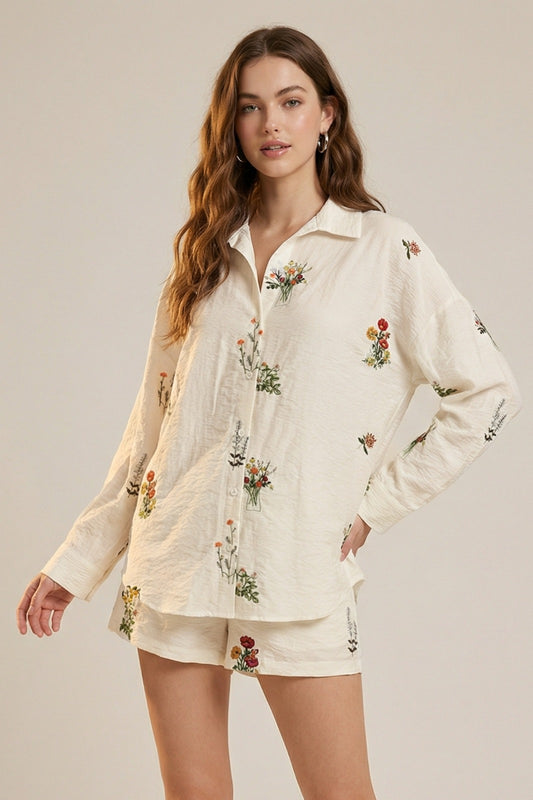 Woman wearing a cream-colored embroidered shirt and shorts set against a neutral background