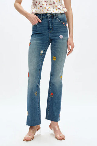 Blue jeans with floral patches worn by a person on a white background