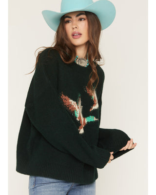 Woman wearing a black sweater with a colorful design and a light blue cowboy hat on a white background