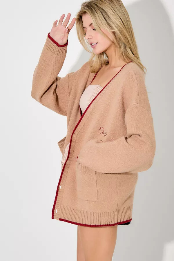 Woman wearing a beige cardigan with red trim on a white background