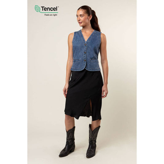 Woman wearing a blue denim vest over a black dress with cowboy boots, Tencel logo visible.