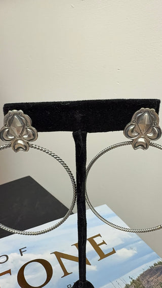 Handmade sterling silver hoop earrings with floral concho tops on black display stand